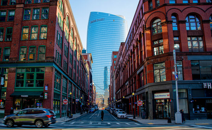 The curved glass State Street tower framed between historic brick buildings on a Boston street