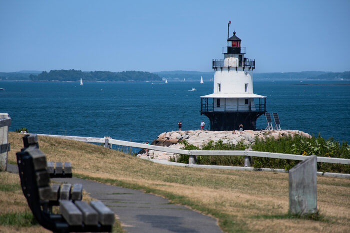 Spring Point Ledge Light lighthouse on a stone breakwater on a clear summer day, with sailboats on Casco Bay behind it